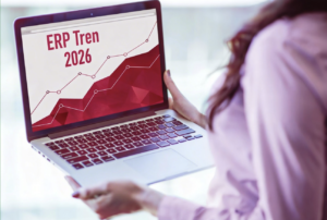Perempuan memegang laptop yang menampilkan grafik pertumbuhan berwarna merah dan judul “Tren ERP 2026” di layar.